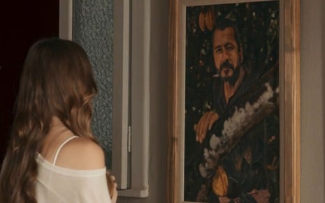 De costas, Gabriela Medeiros como Buba observa um quadro de Marcos Palmeira, o José Inocêncio, pendurado na parede em cena de Renascer